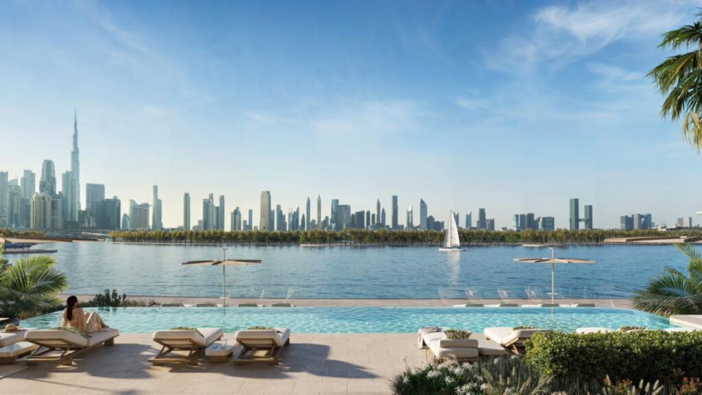 A luxurious pool area with lounge chairs overlooks a calm stretch of water and the city skyline, where tall skyscrapers rise under a clear blue sky, capturing the art of urban living. A sailboat glides by in the distance.