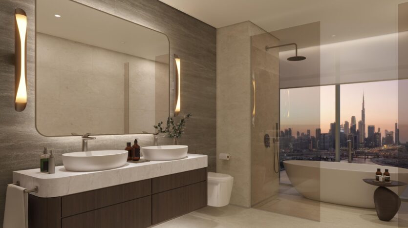 The modern bathroom showcases artistry with double sinks, a large mirror, and wall sconces. The freestanding bathtub and shower are installed near floor-to-ceiling windows overlooking the city skyline at sunset. The colors are neutral and elegant.