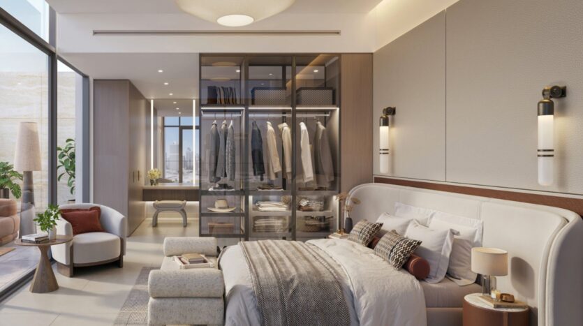 Modern room with a large bed, neutral bedding, a glass-door wardrobe with hanging clothes, an armchair, wall sconces, and floor-to-ceiling windows that let in natural light and offer breathtaking views of the Eltiera.