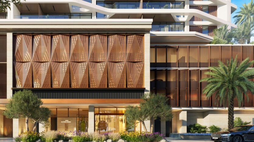 Exterior of a modern building in Eltiera Views, featuring bronze-colored geometric panels, a large glass entrance, green spaces, and palm trees in the foreground, under bright sunshine.
