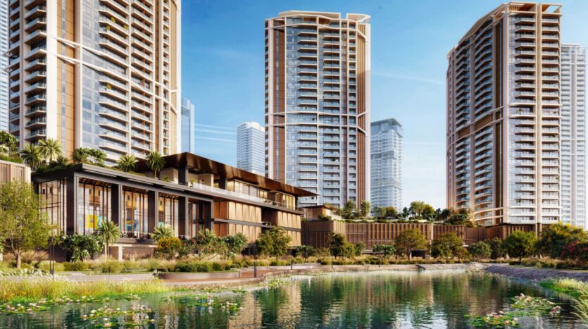 Modern high-rise residential buildings with glass balconies surround a landscaped area at Eltiera Views, featuring greenery, palm trees, and a reflecting pond in the foreground under a clear blue sky.