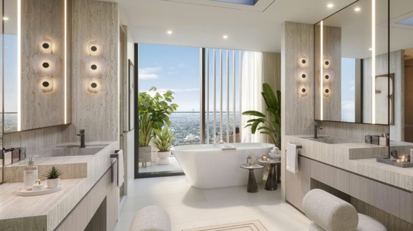 Modern and luxurious bathroom with a freestanding bathtub near large windows, two sinks with mirrors, beige stone surfaces, greenery, and a breathtaking view of the Eltiera in the background. Soft lighting creates a serene atmosphere.
