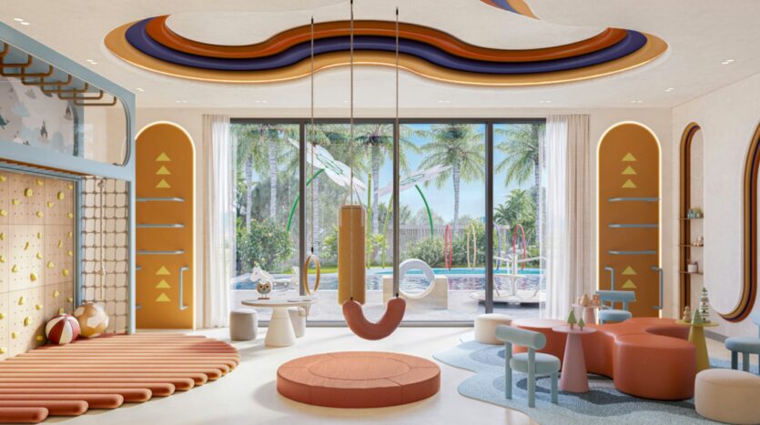 A colorful and modern playroom with climbing structures, round seats, swings, and small tables. Large windows offer Eltiera a view of the palm trees and outdoor pool, filling the space with abundant natural light.