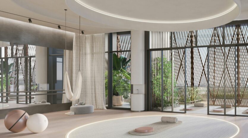 Modern, sunlit yoga studio with large windows overlooking Eltiera Views, hanging swings, yoga mats, exercise balls, and greenery outside. Neutral tones and soft lighting create a calm and welcoming atmosphere.