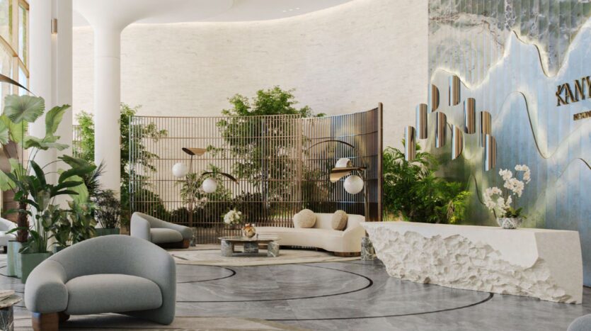 Entrance hall of a modern hotel with elegant curved chairs, a textured white reception desk, lush green plants, stylish lighting, and a decorative wall with gold accents and the word "KANDIMA." Natural light fills this bright space inspired by Kanyon.