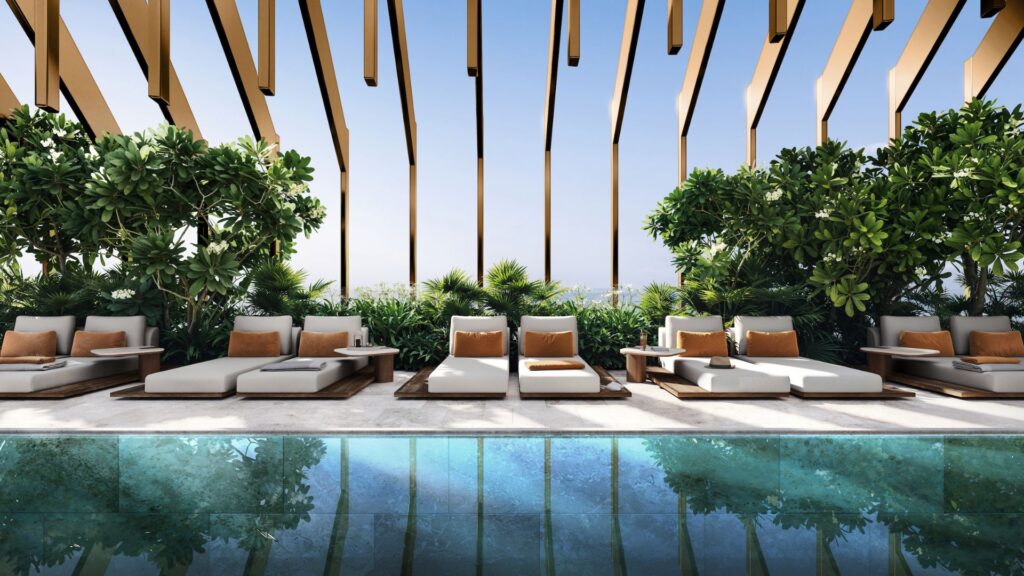 Kanyon's luxurious outdoor lounge with modern upholstered sofas, orange cushions, lush green plants, and a reflective pool under a wooden slatted pergola on a sunny day.