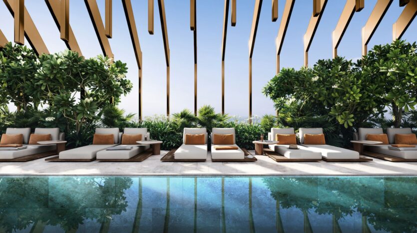 Kanyon's luxurious outdoor lounge with modern upholstered sofas, orange cushions, lush green plants, and a reflective pool under a wooden slatted pergola on a sunny day.