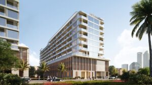 Ein modernes, mehrstöckiges Linea-Hotel mit Glasbalkonen, umgeben von Palmen und Grünflächen, befindet sich in der Nähe einer Straße, auf der Menschen und Autos unterwegs sind. Die Wolkenkratzer der Stadt sind vor dem Hintergrund des klaren Himmels zu sehen.