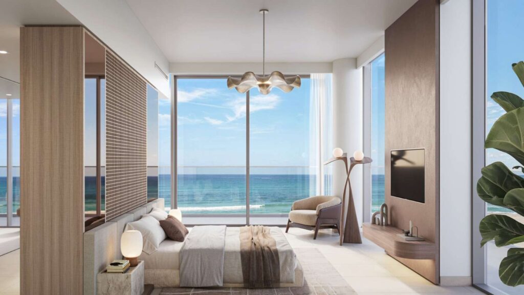Chambre moderne Soto Grande avec des fenêtres allant du sol au plafond et donnant sur l'océan, avec un lit confortable, un décor neutre, une télévision murale, un fauteuil, un lampadaire, une plante et une lumière naturelle abondante.