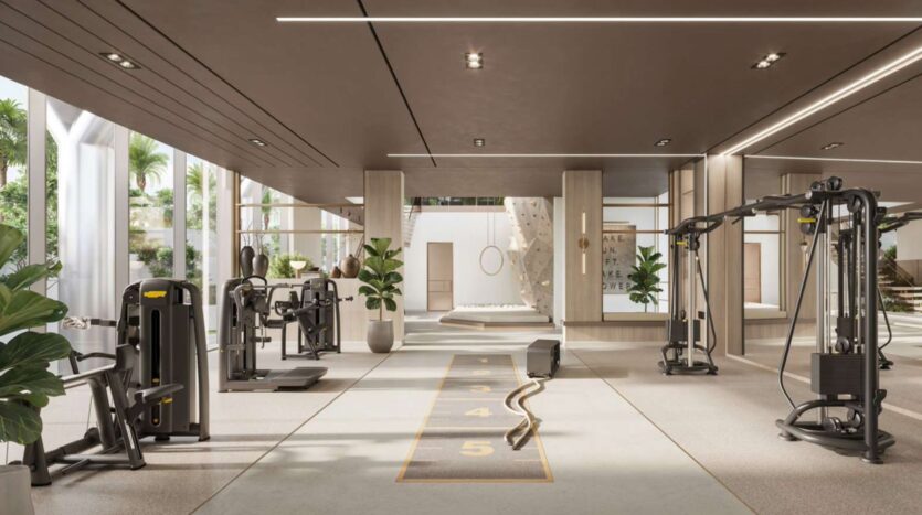 Salle de sport moderne et spacieuse à Soto Grande avec des machines d'exercice, une corde de combat, des plantes luxuriantes et de grandes fenêtres laissant entrer la lumière naturelle. Un mur d'escalade et un panneau de motivation sont visibles à l'arrière-plan.