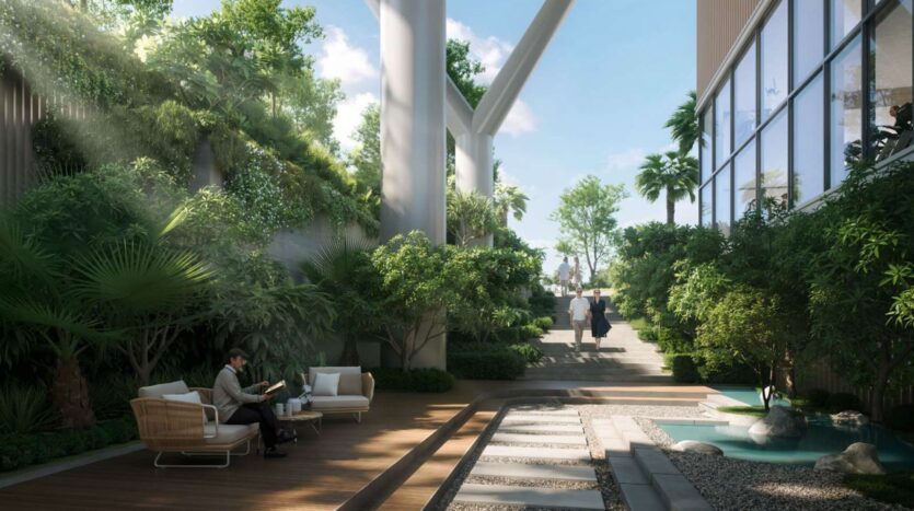 Un salon extérieur moderne à Soto Grande présente une végétation luxuriante, une terrasse en bois, des canapés blancs et un petit étang. La lumière du soleil filtre à travers les plantes tandis que deux personnes marchent sur un sentier à l'arrière-plan.