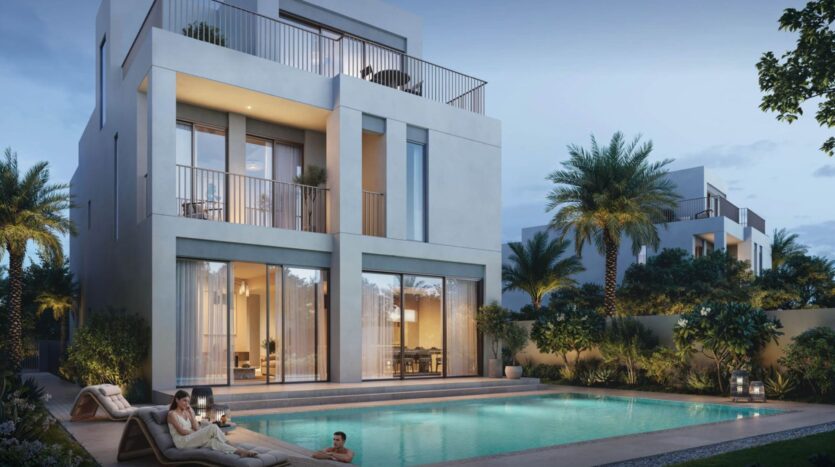 Modern three-story villa in The Heights with large windows, balconies, and a pool at the front. Two people relax on lounge chairs by the pool while another swims. Tropical plants and palm trees surround the property at dusk.