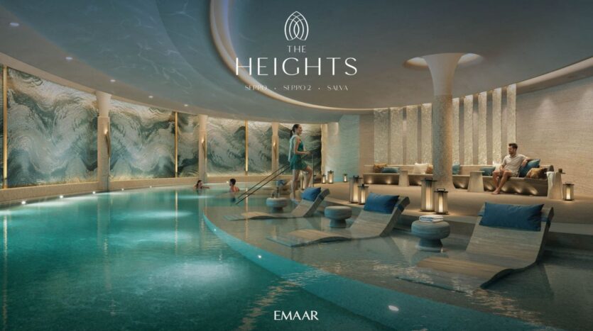 A luxurious indoor pool at The Heights, featuring lounge chairs in the water, people relaxing by the pool, and modern wave-shaped wall art. The tranquil scene is enhanced by soft lighting and elegant décor bearing the "EMAAR" logo.