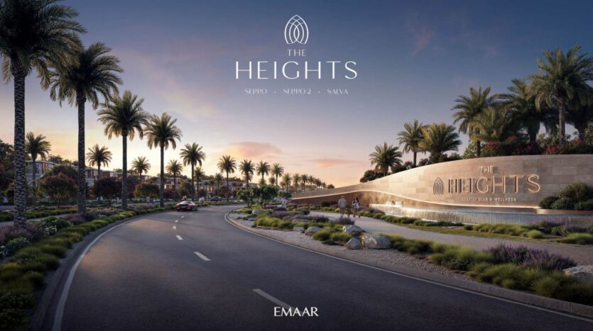 A wide, curved road lined with palm trees leads to the elegant entrance sign for The Heights, designed by Emaar. At sunset, the greenery, lights, and high-end buildings can be seen in the background.