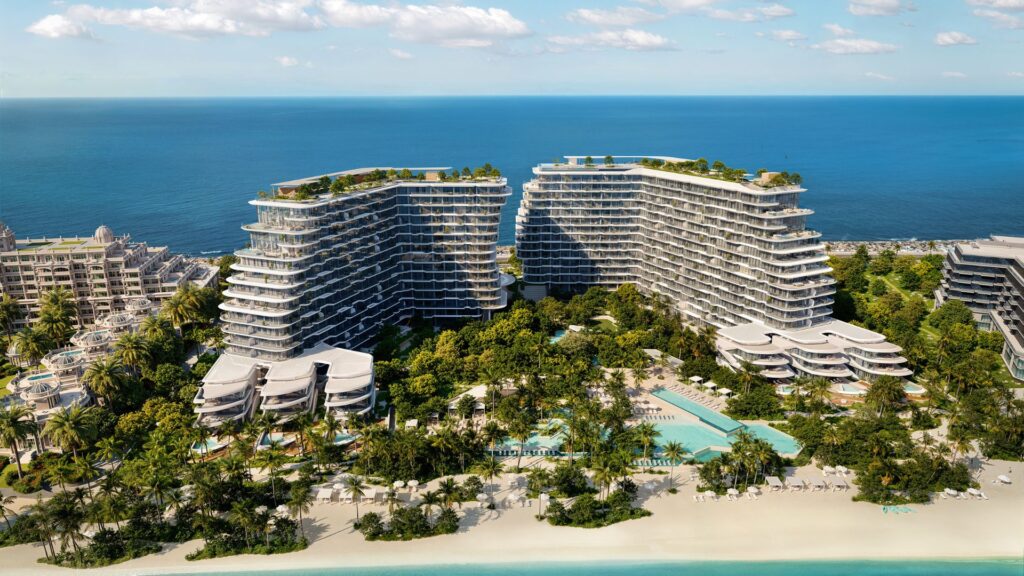 Luftaufnahme der modernen, geschwungenen Gebäude von Bella by Passo, die direkt am Meer liegen und von üppiger Vegetation, Swimmingpools und Entspannungsbereichen umgeben sind. Sie befinden sich in perfekter Lage an einem Sandstrand und dem türkisfarbenen Meer, unter einem blauen Himmel mit vereinzelten Wolken.