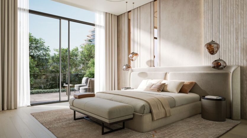 A modern, sunlit bedroom decorated by Bella by Passo, with a large bed, pendant lamps, floor-to-ceiling windows, sheer curtains, a bench at the foot of the bed, and a balcony overlooking the trees.