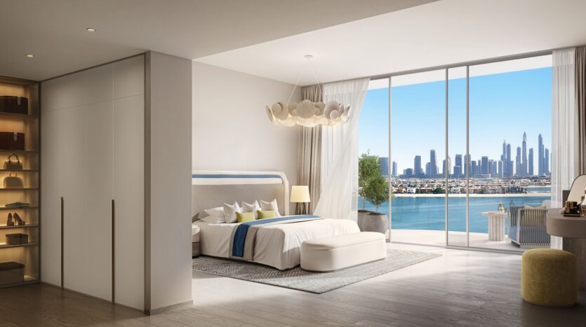 A modern and spacious bedroom by Bella by Passo, featuring large windows overlooking the city skyline and waterfront. The room includes a bed, ottoman, desk, built-in wardrobe, and warm, neutral décor with abundant natural light.