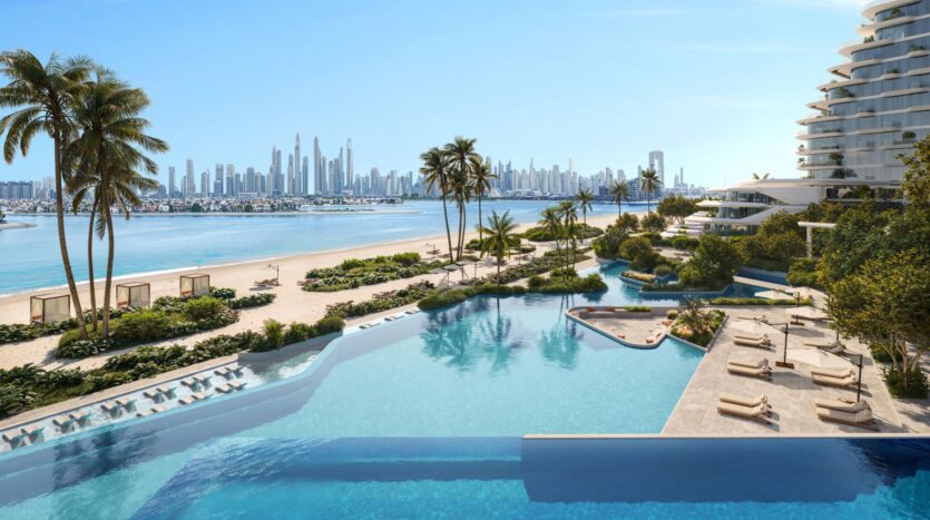 Infinity pool overlooking a sandy beach with palm trees, Bella by Passo luxury cabanas, and a modern city in the background under a clear blue sky. Sun loungers are arranged next to the pool.