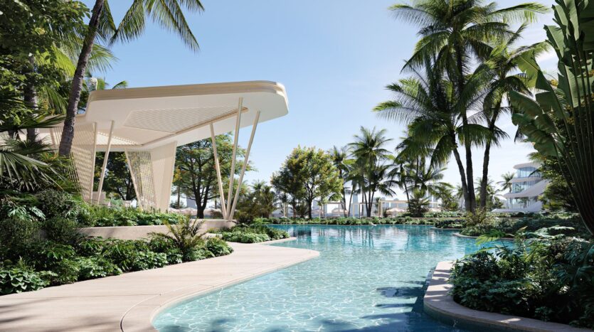 A clear swimming pool surrounded by lush green plants and palm trees, with the modern Bella by Passo pavilion on the left, under a sunny blue sky, creating a tropical seaside resort atmosphere.