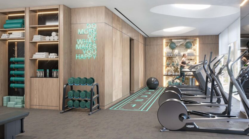 Modern gym in Flora Bay with wooden shelves containing towels and fitness equipment, a neon sign reading "Do more of what makes you happy," treadmills, exercise bikes, and a window showing people working out in the background.