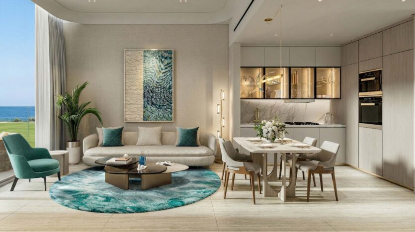 Modern living and dining room in Flora Bay with ocean views, featuring a cream sofa, teal accents, a round blue rug, a dining table for six, and a sleek kitchen with built-in appliances. Large windows flood the space with natural light.