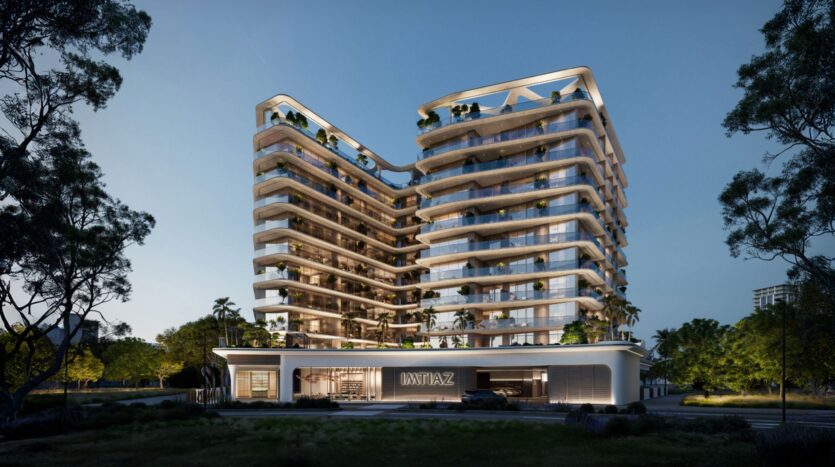 A modern multi-story building with curved glass balconies and green terraces, the Inara residence is illuminated at nightfall. The name "JAZZ" is displayed above the entrance, surrounded by trees and landscaped gardens.