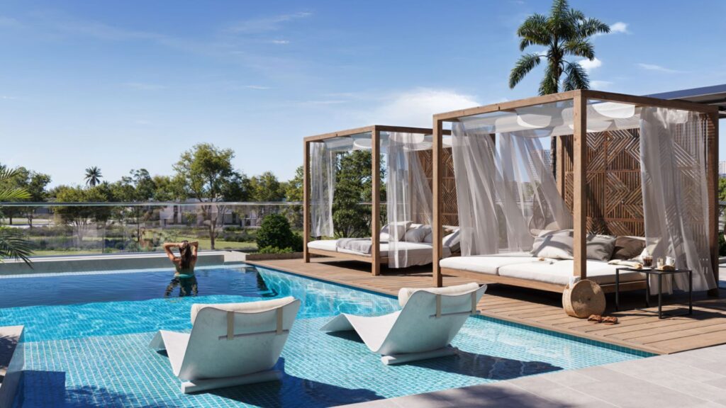 A luxurious scene by the pool at the Inara residence, featuring two shaded cabana beds on a wooden deck, two white lounge chairs in a light blue pool, and a person relaxing in the water, surrounded by palm trees under a bright blue sky.