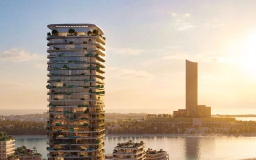 Ein moderner Turm, Le Château, mit geschwungenen Balkonen und üppiger Vegetation, erhebt sich bei Sonnenuntergang am Wasser, während sich im Hintergrund ein weiterer großer Turm über dem ruhigen Wasser erhebt, das die Wärme des Himmels widerspiegelt.