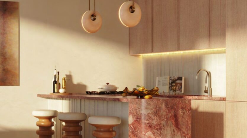 Une cuisine moderne avec un comptoir en marbre rose, trois tabourets rembourrés, des lampes suspendues et un dosseret d'inspiration Le Château avec éclairage sous l'armoire. Des objets décoratifs et des articles de cuisine sont disposés sur le comptoir.