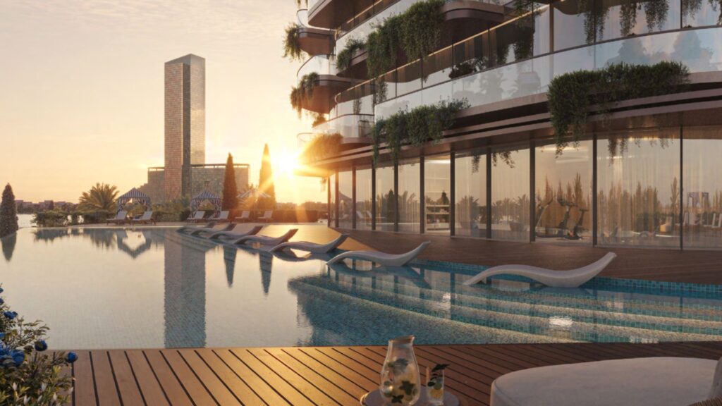 La luxueuse piscine du Château est équipée de chaises longues modernes, d'une terrasse en bois et d'un bâtiment en verre au coucher du soleil. De la verdure orne les balcons, avec un grand gratte-ciel visible en arrière-plan.