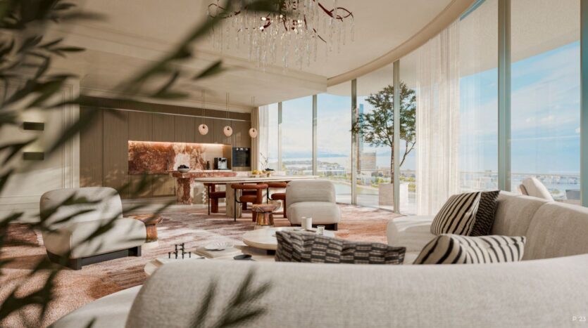 Le salon moderne et ensoleillé, avec ses fenêtres incurvées allant du sol au plafond, ses canapés aux tons neutres et sa table basse ronde, évoque l'élégance du Château. Il est complété par une élégante cuisine ouverte dotée d'un îlot en marbre et de lampes suspendues.