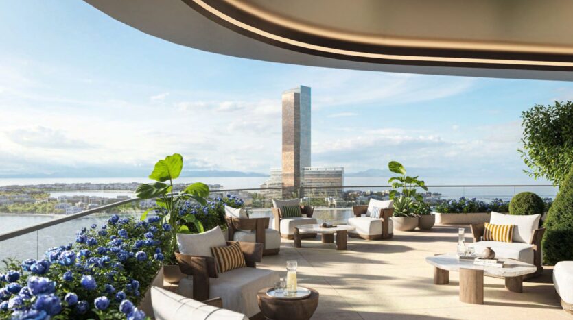 La terrasse moderne du Château, avec ses sièges élégants, ses plantes luxuriantes et ses fleurs bleues, surplombe une rivière et un grand gratte-ciel réfléchissant sous un ciel partiellement nuageux. La scène est lumineuse, spacieuse et accueillante.