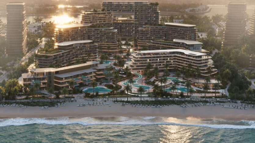 Aerial view of the modern Meriva beach resort, featuring multiple curved buildings, palm trees, winding swimming pools, lounge chairs on the sandy beach, and ocean waves in the foreground at sunset.