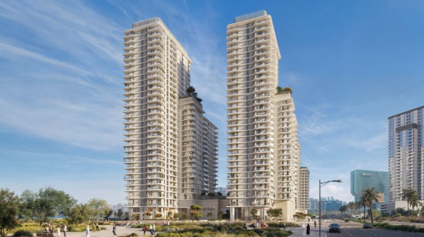 Two modern residential towers with balconies rise up in Muheira, surrounded by greenery, people walking, and urban buildings in the background, under a clear blue sky.