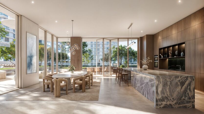 Muheira's modern and spacious kitchen and dining room with a large marble island, round table, wooden cabinets, and floor-to-ceiling windows offering views of the trees and neighboring buildings, all bathed in natural light.