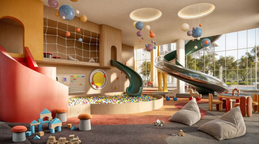 A colorful indoor playroom in Muheira with slides, a ball pit, hanging planet decorations, building blocks, beanbag chairs, and large windows that let in natural light.