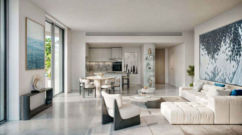 Spacious modern living room with white furniture, large abstract artworks, and an open kitchen. Sunlight streaming in from floor-to-ceiling windows highlights the minimalist Muheira-inspired decor and smooth marble flooring.