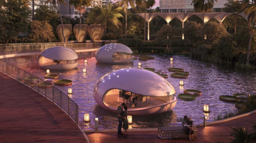 Tre strutture futuristiche a forma di navicella galleggiano su uno stagno con grandi ninfee vicino a Piazza Roma, circondate da piante tropicali ed edifici moderni. Luci calde illuminano la scena mentre una coppia è in piedi su una terrazza di legno in riva al lago.