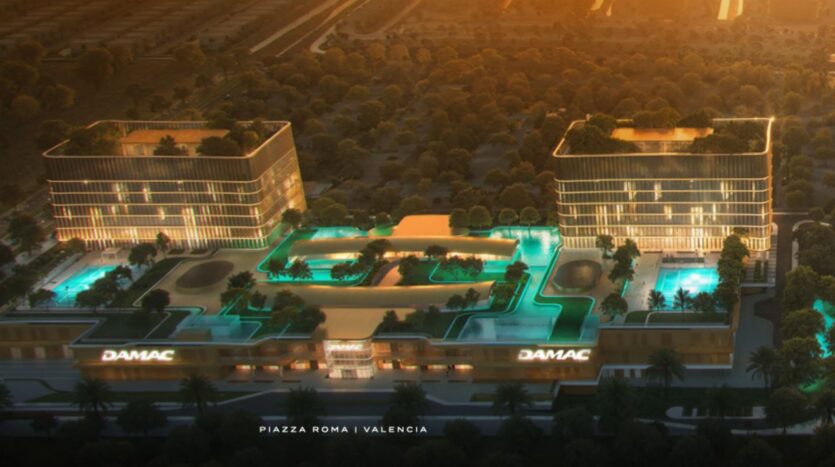 Vista aerea di due moderni edifici in vetro e di una piazza centrale, Piazza Roma, con piscine illuminate, circondate dal verde al tramonto. Gli edifici recano la scritta "DAMAC" e l'indicazione "Piazza Roma | Valencia".