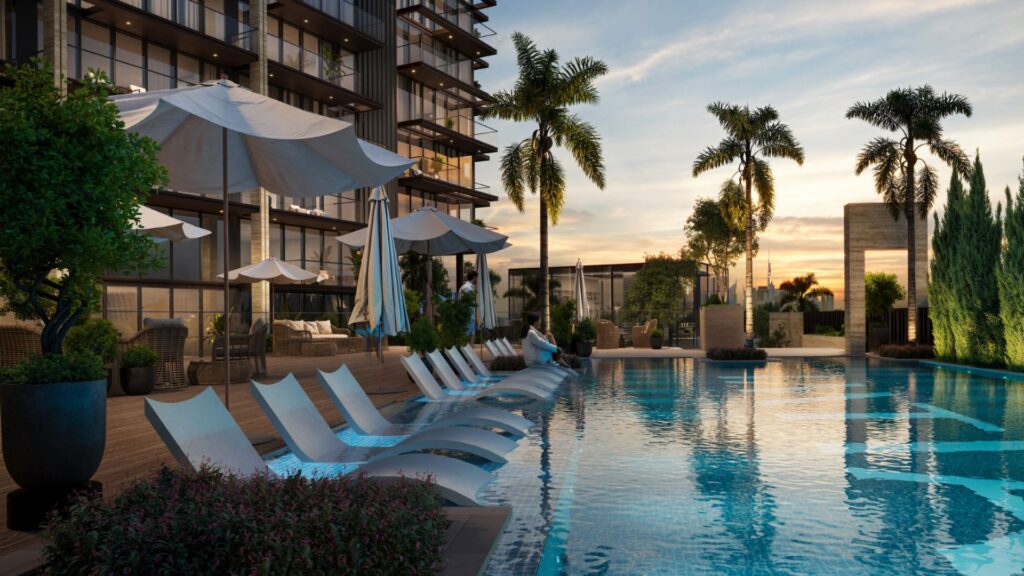 Modern outdoor pool at sunset in Sea Cliff, with lounge chairs partially submerged in the water, large white umbrellas, palm trees, and a contemporary apartment building in the background, all surrounded by lush vegetation.