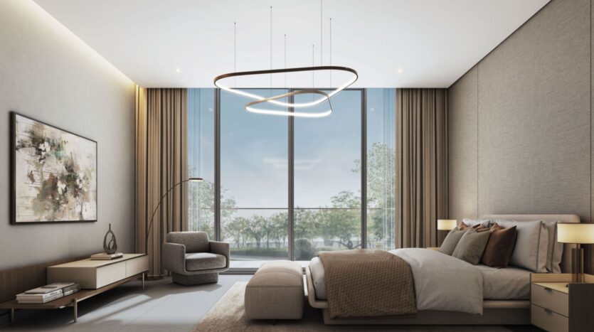 A modern bedroom at Sobha Sanctuary features a large bed with neutral-toned bedding, an armchair, artwork on the walls, a contemporary chandelier, and floor-to-ceiling windows overlooking lush trees and greenery.