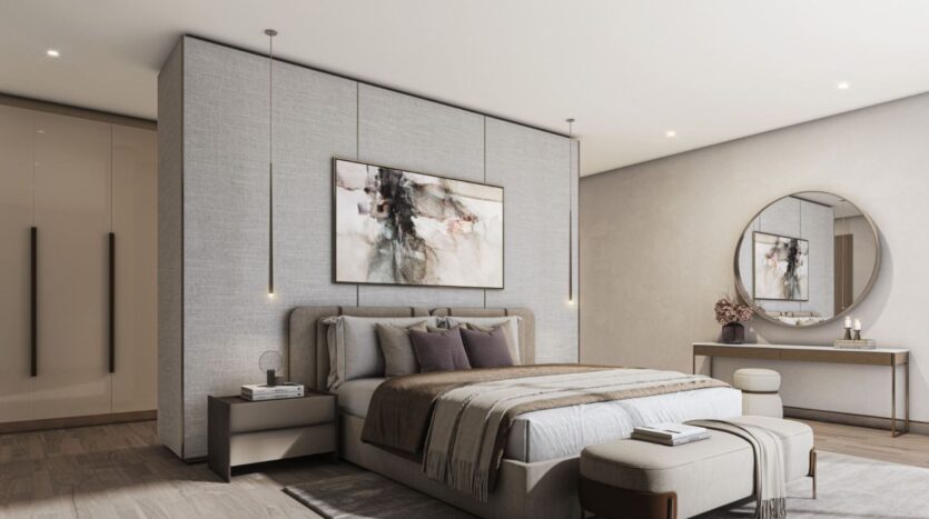 A modern bedroom at Sobha Sanctuary features a large bed with neutral-toned bedding, an abstract painting hanging on the wall, pendant lamps, a round mirror above a console table, and an elegant bench at the foot of the bed.