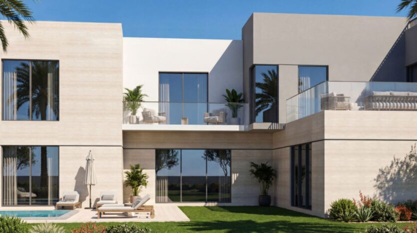 Modern two-story house in Sobha Sanctuary with large bay windows, a spacious balcony with outdoor seating, lounge chairs by the pool, and a well-maintained garden with palm trees and green grass under a clear blue sky.