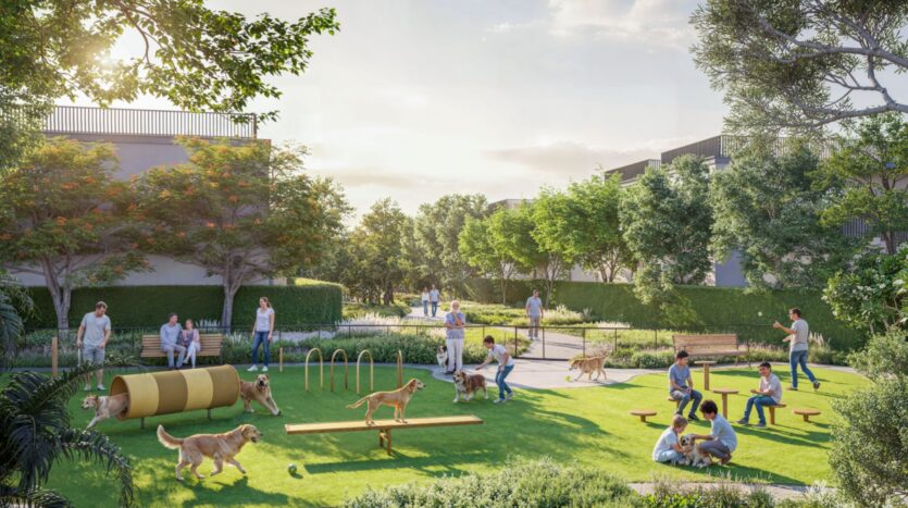 A lively dog park at Sobha Sanctuary with people and dogs playing on agility equipment, sitting on benches, and walking along the trails. The park is surrounded by greenery and trees under a bright, partly cloudy sky.