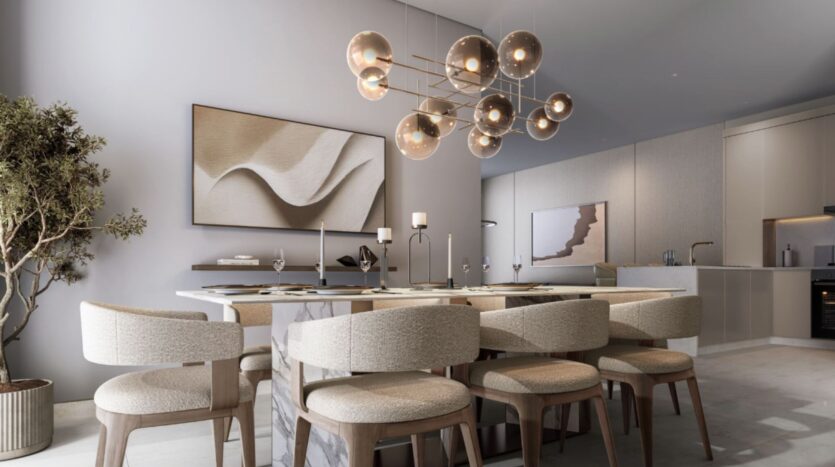 The modern dining room at Sobha Sanctuary features a rectangular table, eight beige upholstered chairs, a sculptural chandelier with globe lights, abstract wall art, a potted tree, and an open kitchen in the background.