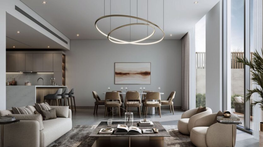 Modern living and dining room at Sobha Sanctuary with neutral colors, large windows, a circular chandelier, plush sofas, a long dining table with chairs, wall art, and a stylish kitchen with bar stools in the background.