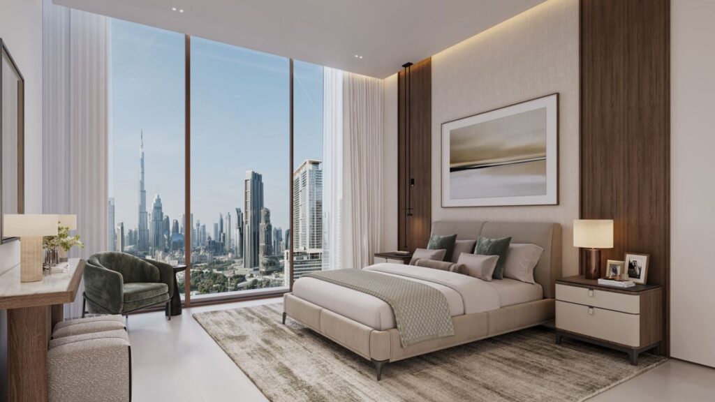 Современная комната в The Residences DIFC с большими окнами, из которых открывается вид на горизонт города, включая высокие небоскребы. В комнате есть кровать, прикроватные тумбочки с лампами, ковер, кресло и нейтральный декор с зелеными и бежевыми акцентами.