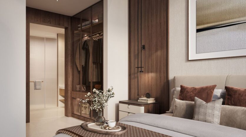 Современная спальня в The Residences DIFC оформлена в нейтральных тонах и обставлена кроватью с коричневыми подушками, тумбочкой, вазой с цветами и подносом с чаем. Открытый шкаф и ванная комната украшены элегантными деталями из дерева и стекла.