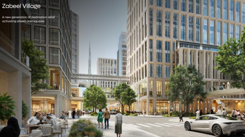 Современная городская площадь в Zabeel Village с высокими зданиями, такими как The Residences DIFC, магазинами, деревьями, прогуливающимися людьми и припаркованным белым спортивным автомобилем. На заднем плане возвышается небоскреб Бурж-Халифа.