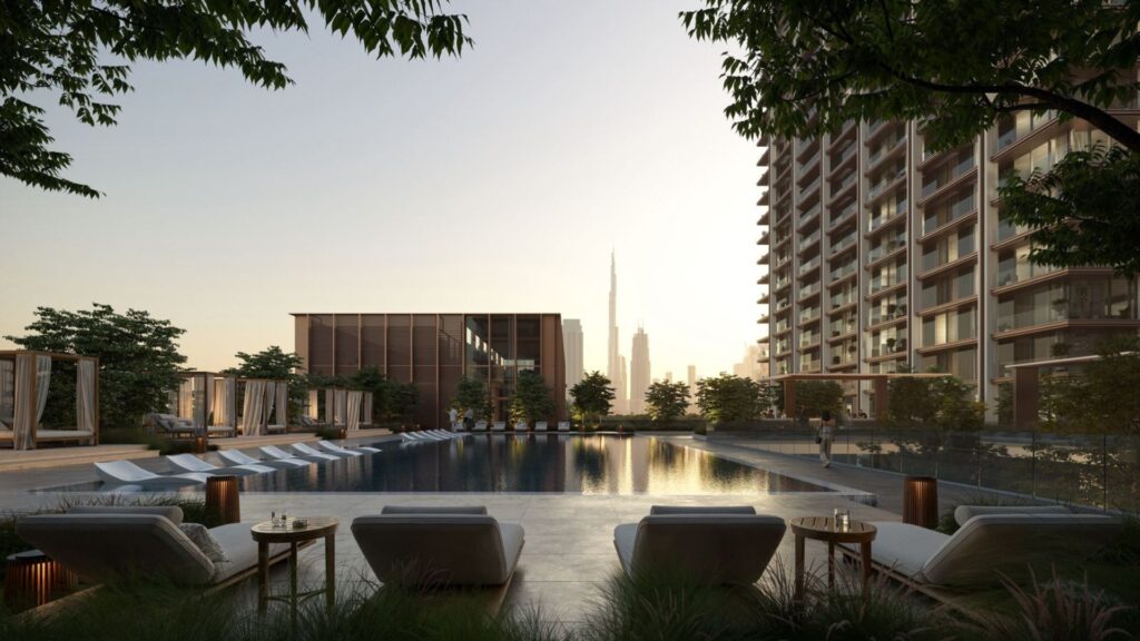 Современный открытый бассейн The Residences DIFC, окруженный большим жилым зданием и зелеными насаждениями, оборудован шезлонгами и беседками. Из него открывается вид на горизонт города с выделяющимся на фоне заката небоскребом.
